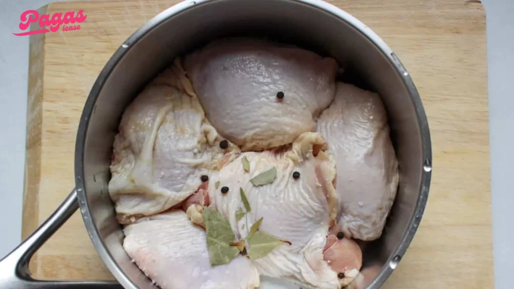 Chicken thighs boiling with peppercorns and bay leaves for tender results.